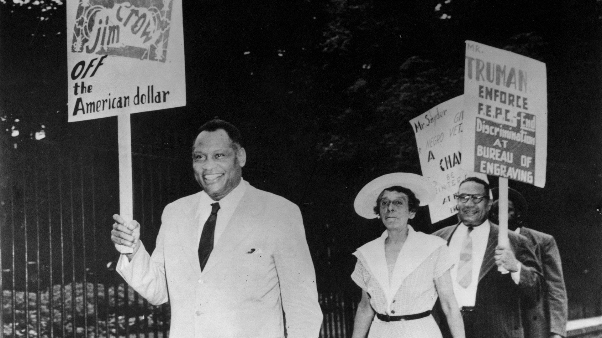 Paul Robeson walking with banner at anti-segregation march 1948