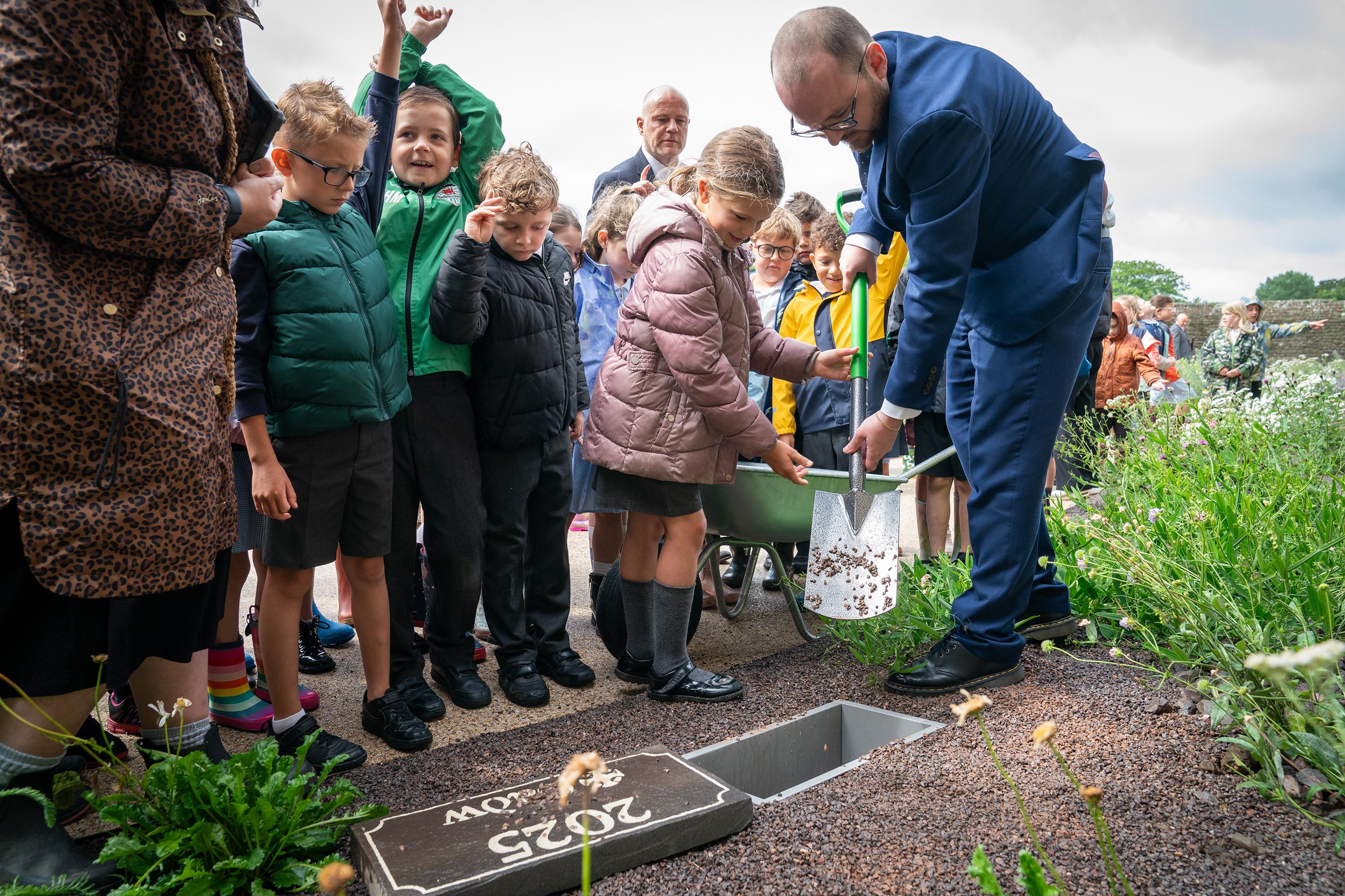 Minister for Culture Jack Sargent burying time capsule with children from Ysgol Y Castell 